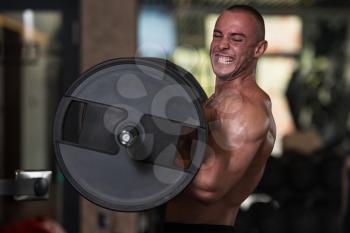 Muscular Man Doing Heavy Weight Exercise For Biceps With Barbell In Gym