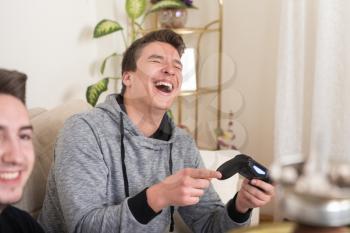 Two Brothers or Friends Playing Video Games Together as They Relax on a Couch in the Living Room