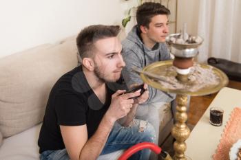 Two Young Gamers Sitting Together On Sofa And Playing Video Games At Home