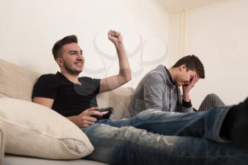 Two Brothers or Friends Playing Video Games Together as They Relax on a Couch in the Living Room