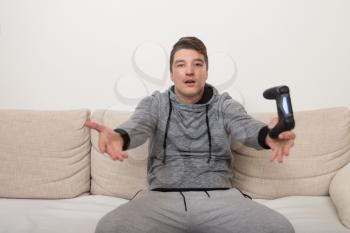 Young Gamer Sitting On Sofa And Playing Video Games At Home