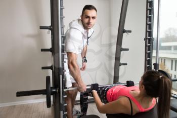 Personal Trainer Showing Young Woman How To Train Legs On Machine In The Gym