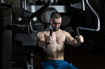 Handsome Muscular Fitness Man Wearing Glasses Doing Heavy Weight Exercise For Chest On Machine With Cable In The Gym