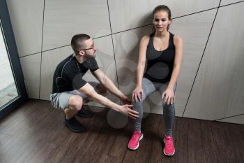 Young Woman And Personal Trainer Exercising Legs Leaning on the Wall In Gym