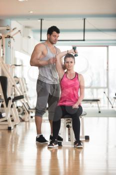 Personal Trainer Showing Young Woman How To Train Triceps Exercise With Dumbbell In A Health And Fitness Concept