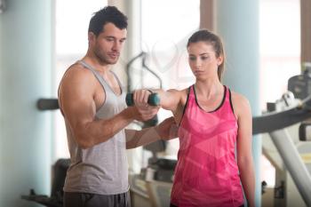 Personal Trainer Showing Young Woman How To Train Shoulder Exercise With Dumbbells In A Gym