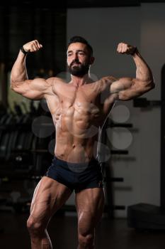 Handsome Young Man Standing Strong In The Gym And Flexing Muscles - Muscular Athletic Bodybuilder Fitness Model Posing After Exercises