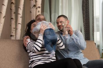 Relaxed Young Couple With Cute Little Baby Sitting on Couch Playing and Laughing