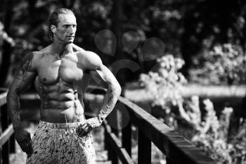 Handsome Mature Man Standing Strong Outdoors In Nature And Flexing Muscles - Muscular Athletic Bodybuilder Fitness Model Posing After Exercises