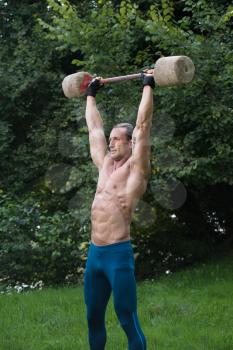 Muscular Adult Man Doing A Exercise For Shoulders With Made Hand Barbell Outdoors Workout