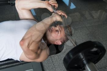 Muscular Man Doing Heavy Weight Exercise For Triceps With Barbell In Gym