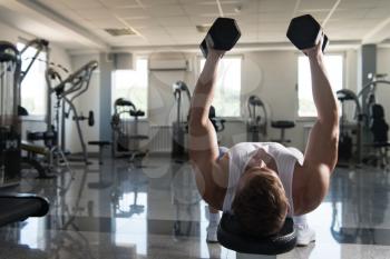 Muscular Young Man Doing Heavy Weight Exercise For Chest With Dumbbells In Modern Fitness Center Gym