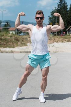 Healthy Young Man Standing Strong Outdoors  And Flexing Muscles - Muscular Athletic Bodybuilder Fitness Model Posing After Exercises