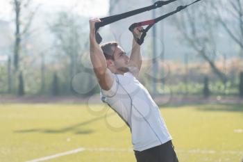 Attractive Man Doing Crossfit With Trx Fitness Straps in City Park Area - Training and Exercising for Endurance - Healthy Lifestyle Concept Outdoor