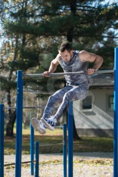 Attractive Man Doing Crossfit Exercise With Dips Bar in City Park Area - Training and Exercising for Endurance - Healthy Lifestyle Concept Outdoor