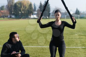 Young Couple Doing Crossfit With Trx Fitness Straps in City Park Area - Training and Exercising for Endurance - Healthy Lifestyle Concept Outdoor