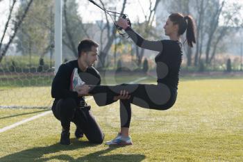 Young Couple Doing Crossfit With Trx Fitness Straps in City Park Area - Training and Exercising for Endurance - Healthy Lifestyle Concept Outdoor