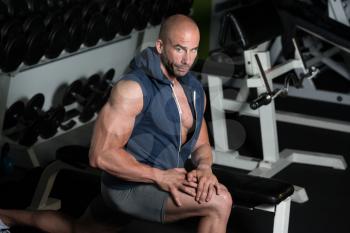 Muscular Man Stretching His Leg At The Floor In A Gym And Flexing Muscles - Muscular Athletic Bodybuilder Fitness Model