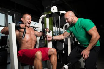 Mature Man Working Out In Gym - Doing Chest Exercise On Machine With Help Of His Trainer