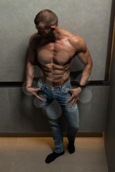 Portrait of a Young Physically Fit Man Showing His Well Trained Body While Wearing Blue Jeans - Muscular Athletic Bodybuilder Fitness Model Posing After Exercises on Wall Near the Wall - a Place for Your Text