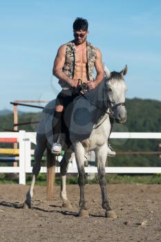 Handsome Macho Man Cowboy Riding on a Horse - Background of Sky and Mountains