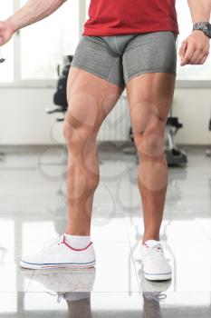 Healthy Young Man Standing Strong In The Gym And Flexing Legs close Up - Muscular Athletic Bodybuilder Fitness Model Posing After Exercises