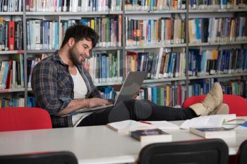 Handsome Man With Dark Hair Sitting at a Desk in the Library - Laptop and Organiser on the Table - Looking at the Screen a Concept of Studying - Blurred Books at the Back