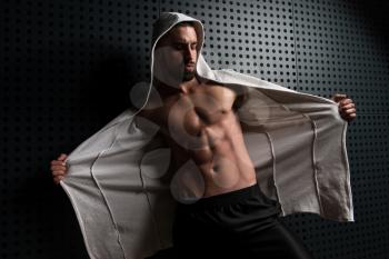Healthy Young Man Standing Strong Standing Against a Wall and Flexing Muscles In Sweatshirt - Muscular Athletic Bodybuilder Fitness Model Posing After Exercises - a Place for Your Text