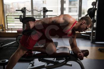 Muscular Young Man Doing Heavy Weight Exercise For Triceps With Dumbbells In Modern Fitness Center Gym