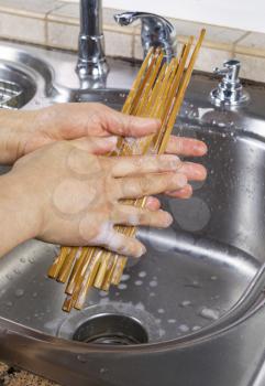 Vertical photo of female hands cleaning bamboo chopsticks with soapy water along with kitchen sink and faucet in background