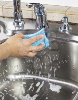 Vertical photo of female hand cleaning kitchen sink with soapy sponge