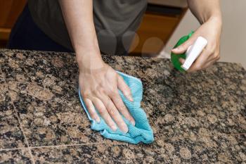 Hands with rag and spray bottle cleaning stone counter-top