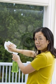 Asian woman cleaning window with spray bottle and paper towel in hand