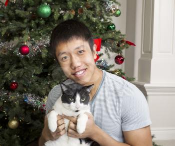 Young Adult Man and old family cat with Christmas tree in background