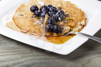 Blueberry pancakes with lot's of maple syrup on white plate with fork 