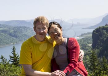 Horizontal photo of mature interracial couple holding each other with the Columbia River Gorge located in the Northwest section of the United States in the background