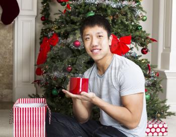 Young man with coffee mug as holiday gift with decorated tree in background