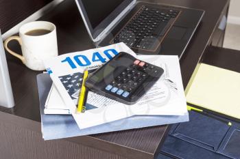 Pile of tax returns with computer, cup of coffee and calculator on desk