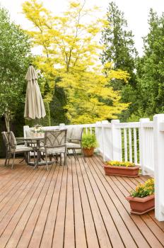 Vertical photo of a large outdoor natural cedar deck with patio furniture and bright yellow and green trees in background