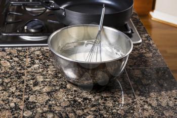 Pancake batter in stainless steel bowl with whisk and stove top in background