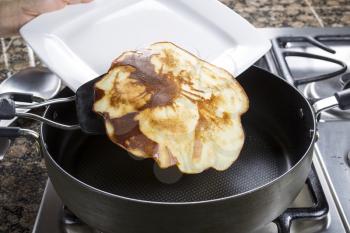Horizontal photo of focus on pancake coming out of frying pan and on to plate