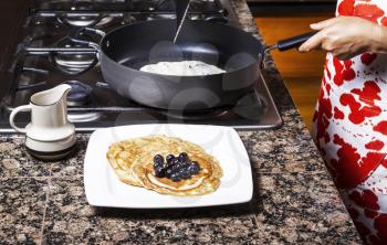 Freshly made pancakes with blueberries on top with frying pan in background