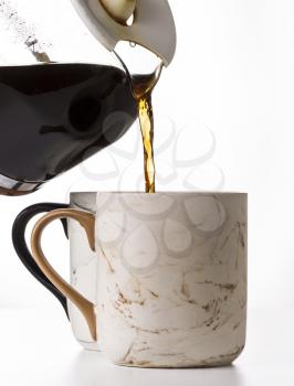 Pouring fresh coffee into porcelain mug on white background