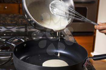 Pouring  pancake batter into frying pan with stove top in background