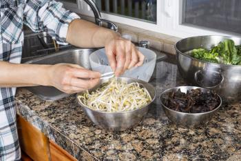 Horizontal photo of female Hands cleaning bean sprouts, with Chinese wood ears, and Choy on top of kitchen counter next to stainless steel sink with plastic strainer
