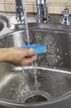 Vertical photo of female hand rinsing soapy sponge with water running out of faucet