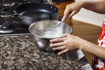 Hand whisking pancake batter on gas stove with kitchen floor and counter top in background
