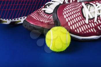 Tennis shoes, new ball, and racket on blue background