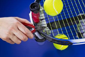 Hand holding pliers while trimming string on tennis racket  on blue background