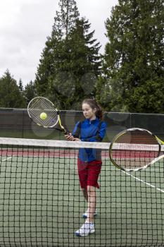 Young girl taking volley against opponent at the net with green trees in background